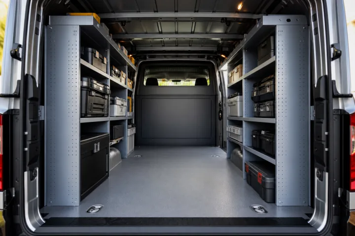 Inside of a work van with side shelving, secured tool cases and a bulkhead behind the front seats.