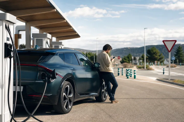 Electric car parked beside public chargers at a Spanish service area while a person checks the route on a phone.