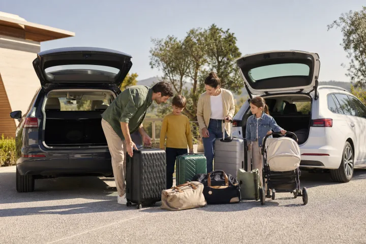 Family comparing the boot space of two cars with suitcases and a pushchair beside them.