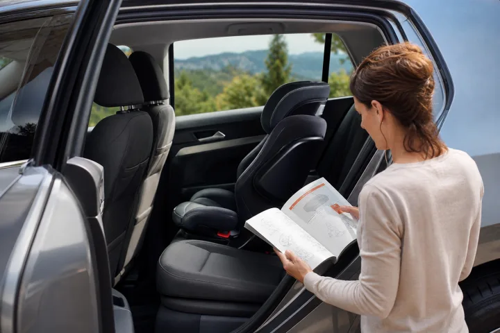 Adult consulting a car manual beside a child car seat fitted on a rear seat