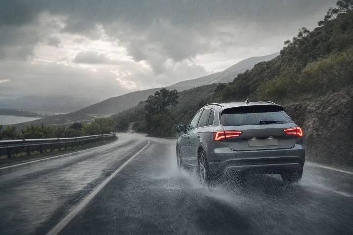 Passenger car travelling slowly on a wet road in rain, with its lights on and a large gap to the vehicle ahead