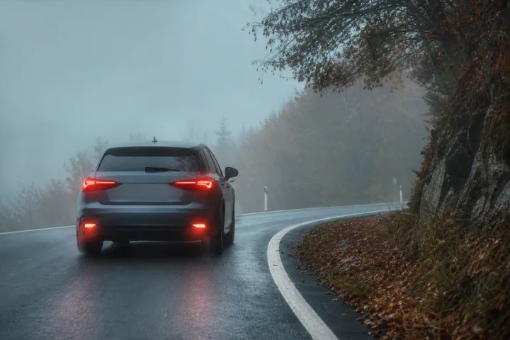 Passenger car driving slowly through dense fog on a road, guided by the white line along the right-hand shoulder.