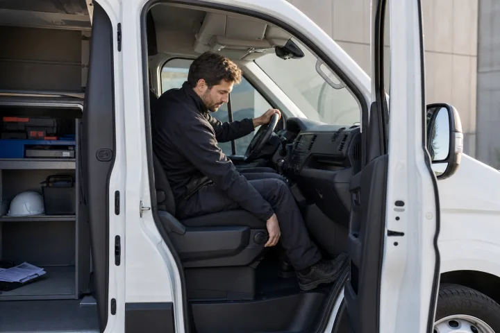 Driver adjusting the seat and steering wheel in the cab of a parked work van